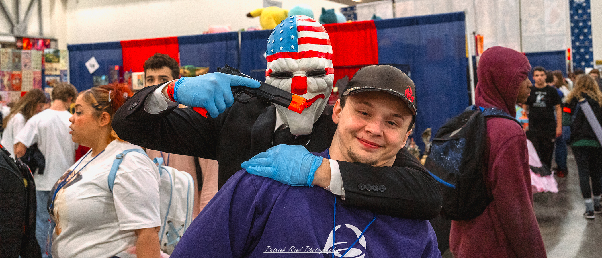 "Cosplayer portraying the Joker from DC Comics, holding a mock hostage—clad in disheveled attire with a playful yet menacing demeanor, maintaining a theatrical expression that captures the chaotic essence of the character."